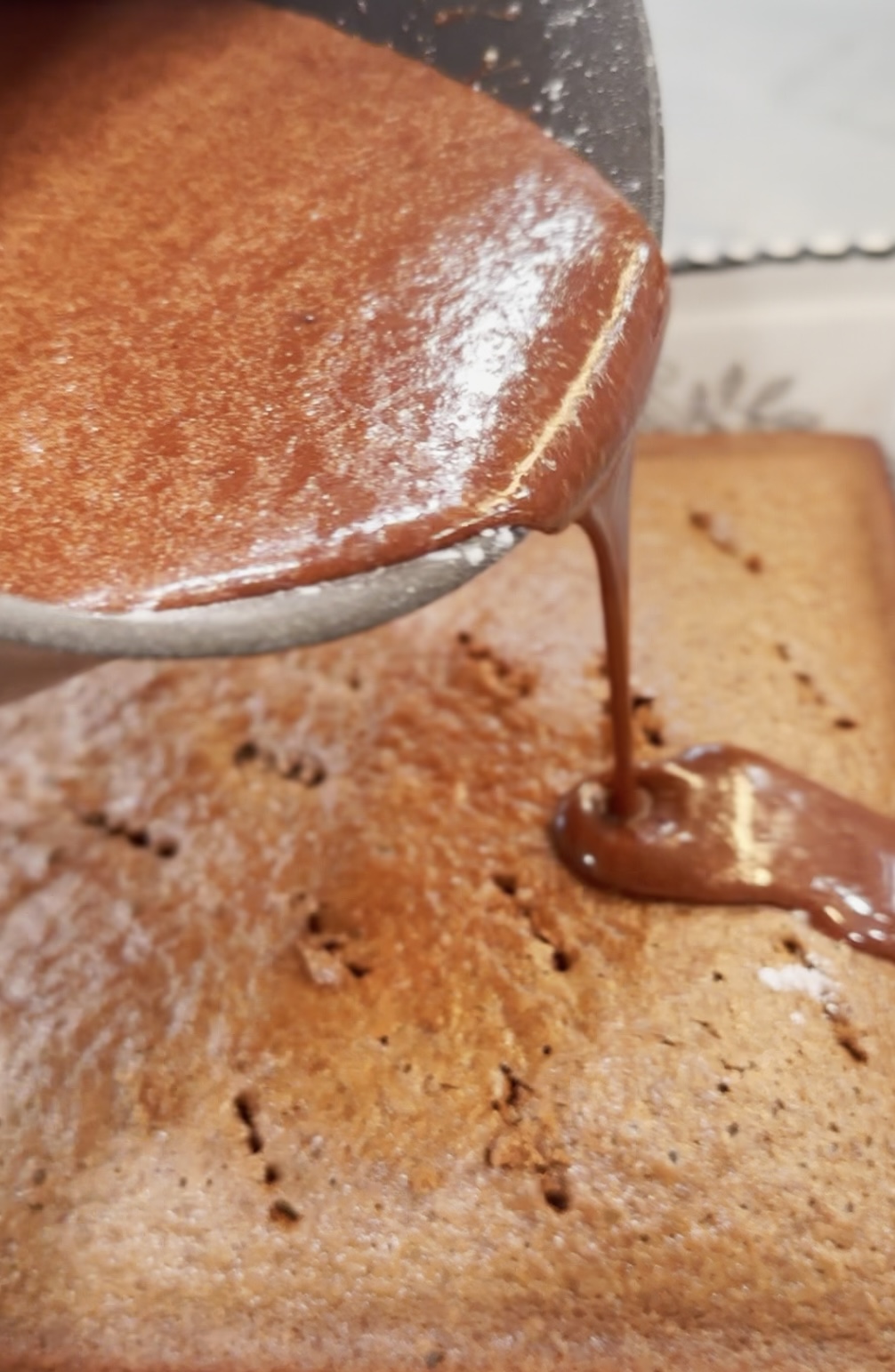 Drizzling warm, chocolate icing onto the hot cake.